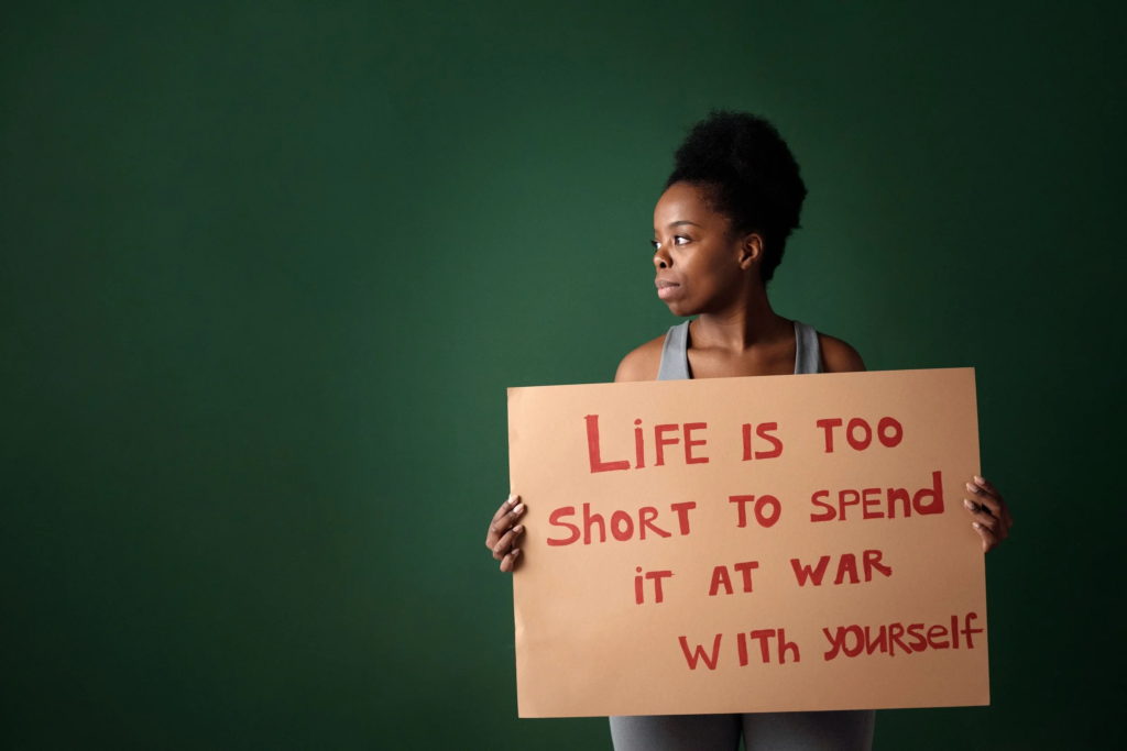 Woman holding a sign that reads “Life is too short to spend it at war with yourself"